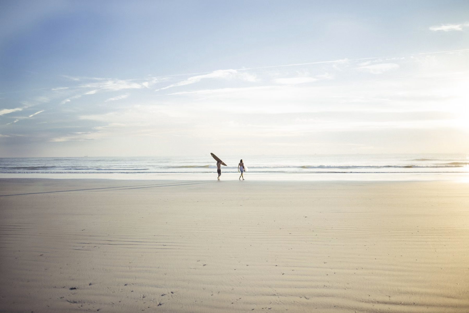 Two people standing near the shoreline in bright daylight, not touching